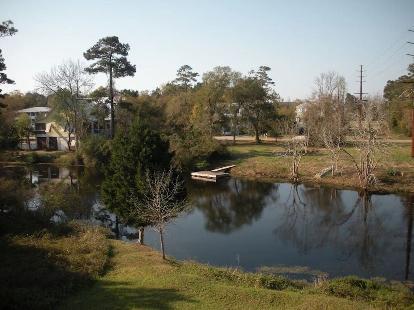 A serene lakeside setting with a dock, surrounded by trees and residential buildings.