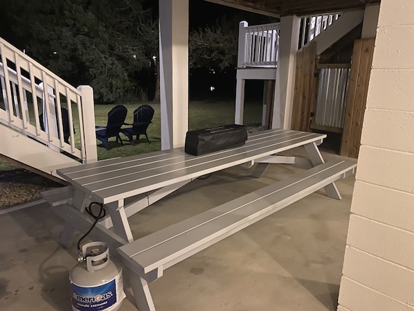An outdoor patio with a picnic table, two Adirondack chairs, a grill, and a propane tank.