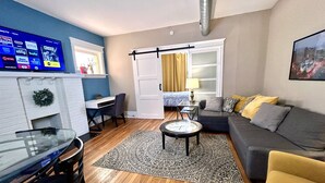 Un espace de vie compact comprenant un téléviseur diffusant des services de streaming, un coin repas avec une table en verre, un canapé avec des coussins et un tapis à motifs.