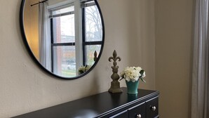 Une commode en bois foncé, surmontée d’un miroir, un vase avec des fleurs blanches et un objet décoratif.