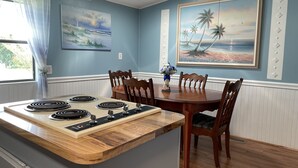 Zona pranzo con tavolo in legno, quattro sedie e piano cottura integrato.