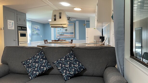 Una cucina moderna con isola centrale, zona pranzo con tavolo e sedie e un divano grigio con cuscini decorati.