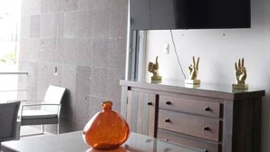 Una habitación moderna con un televisor de pantalla plana grande montado en la pared, un mueble de madera con cajones y una mesa de vidrio con un florero.
