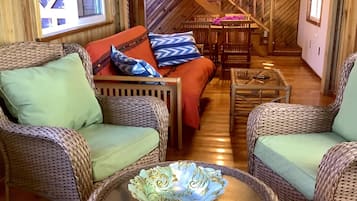 A cozy room with wicker furniture, a glass coffee table, and a staircase leading to an upper level.
