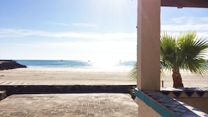 A beach view from a covered patio with a palm tree and tiled flooring.