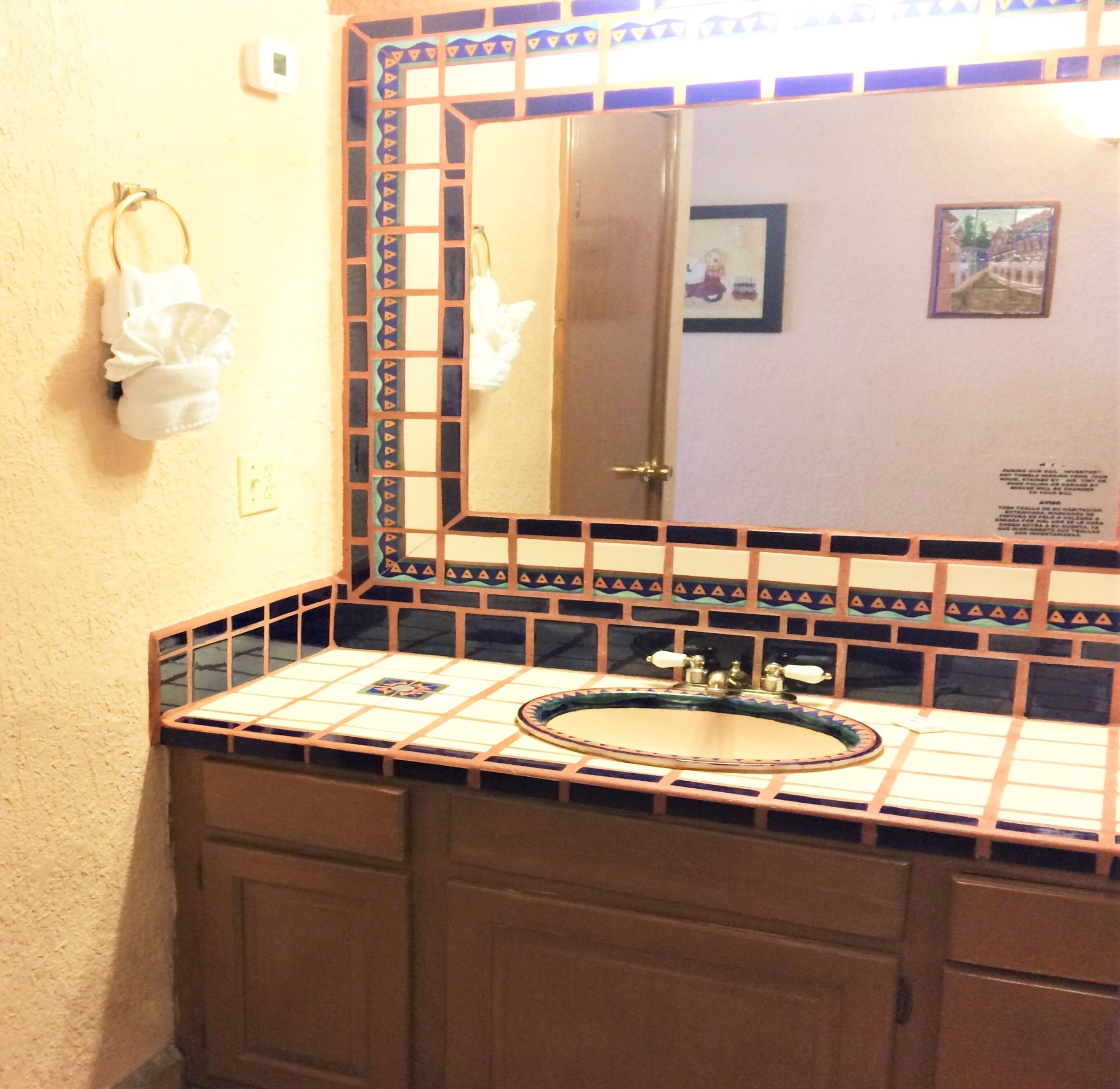 Un baño con lavamanos con azulejos, un espejo con marco decorativo y un perchero para toallas.