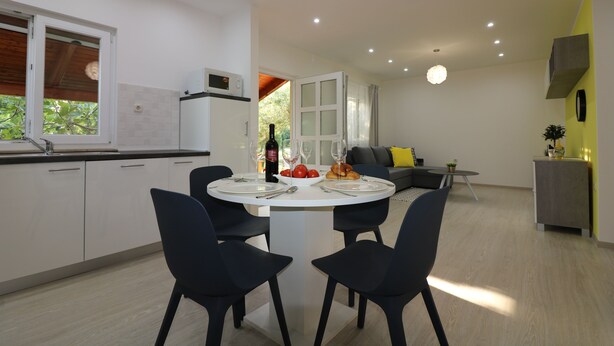 A modern kitchen with white cabinets, a dining table with four chairs, and a view of the living area with a sofa and a small table. - Vacation apartment Bungalow Melisa 5 with pool (POREC)