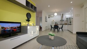 A modern living room with a flat-screen TV, a dining area with a table and chairs, and a kitchen in the background. - Vacation apartment Bungalow Melisa 5 with pool (POREC)