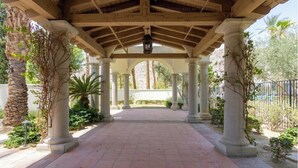 A covered walkway with columns and a lantern, surrounded by greenery and palm trees. - Relaxing Desert Villa in Resort Style property (La Quinta)