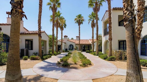 A courtyard with palm trees, a central pathway, and a building with a tiled roof and arched windows. - Relaxing Desert Villa in Resort Style property (La Quinta)