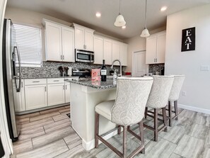 A modern kitchen with white cabinets, a granite countertop, a built-in microwave, and a bar area with patterned stools.
