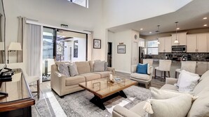 Uma sala de estar espaçosa com um sofá grande, uma mesa de centro e vista para a cozinha e área externa.