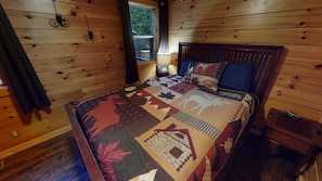 A wooden cabin bedroom with a bed, a nightstand, a lamp, and a window. - Serendipitous Luxury Cabin with Forest Views, Hot Tub, mins from Hocking Hills (Logan)