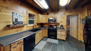 A wooden cabin interior with a kitchen featuring a stove, microwave, and sink. - Serendipitous Luxury Cabin with Forest Views, Hot Tub, mins from Hocking Hills (Logan)