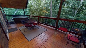 Une terrasse en bois, agrémentée d’une table et de chaises, entourée d’une rambarde et offrant une vue sur une zone boisée.