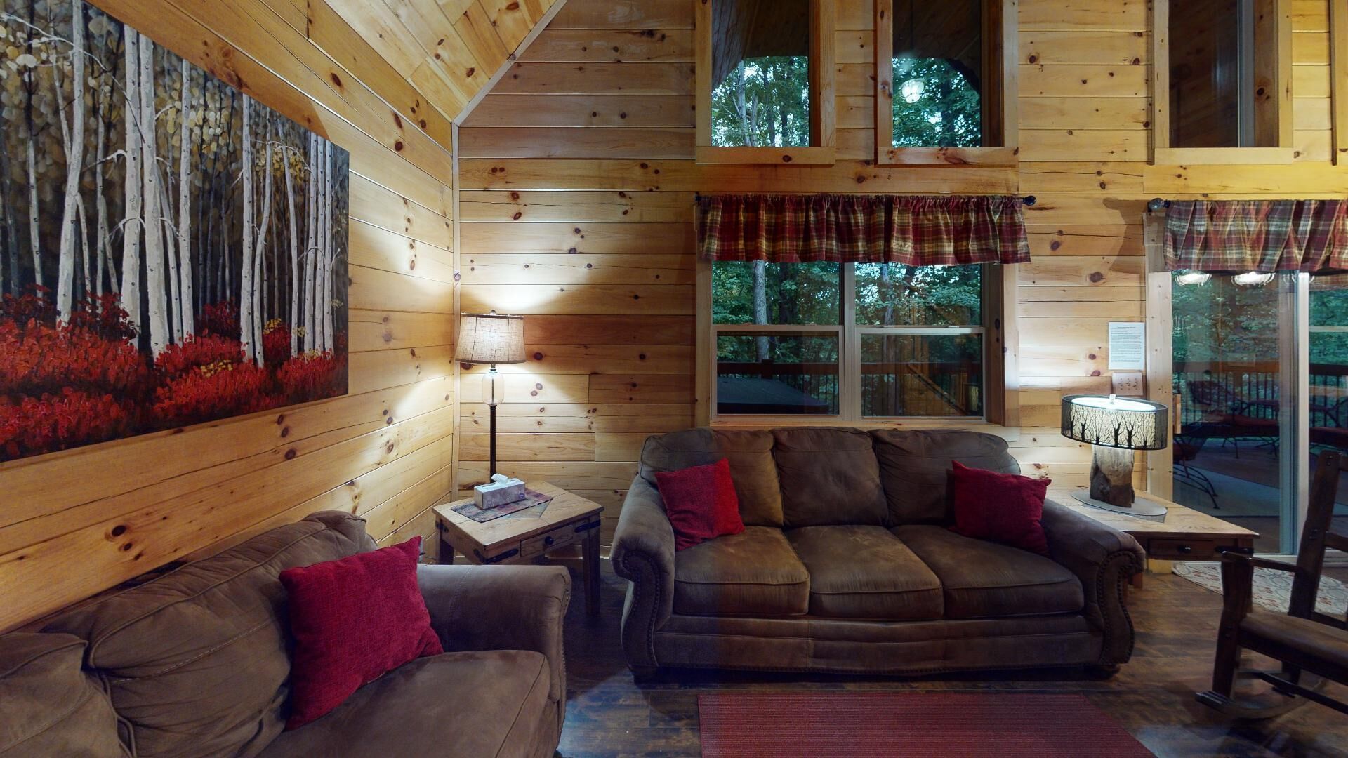 A cozy cabin interior with a wooden interior, a sofa, a table, and a painting of trees.