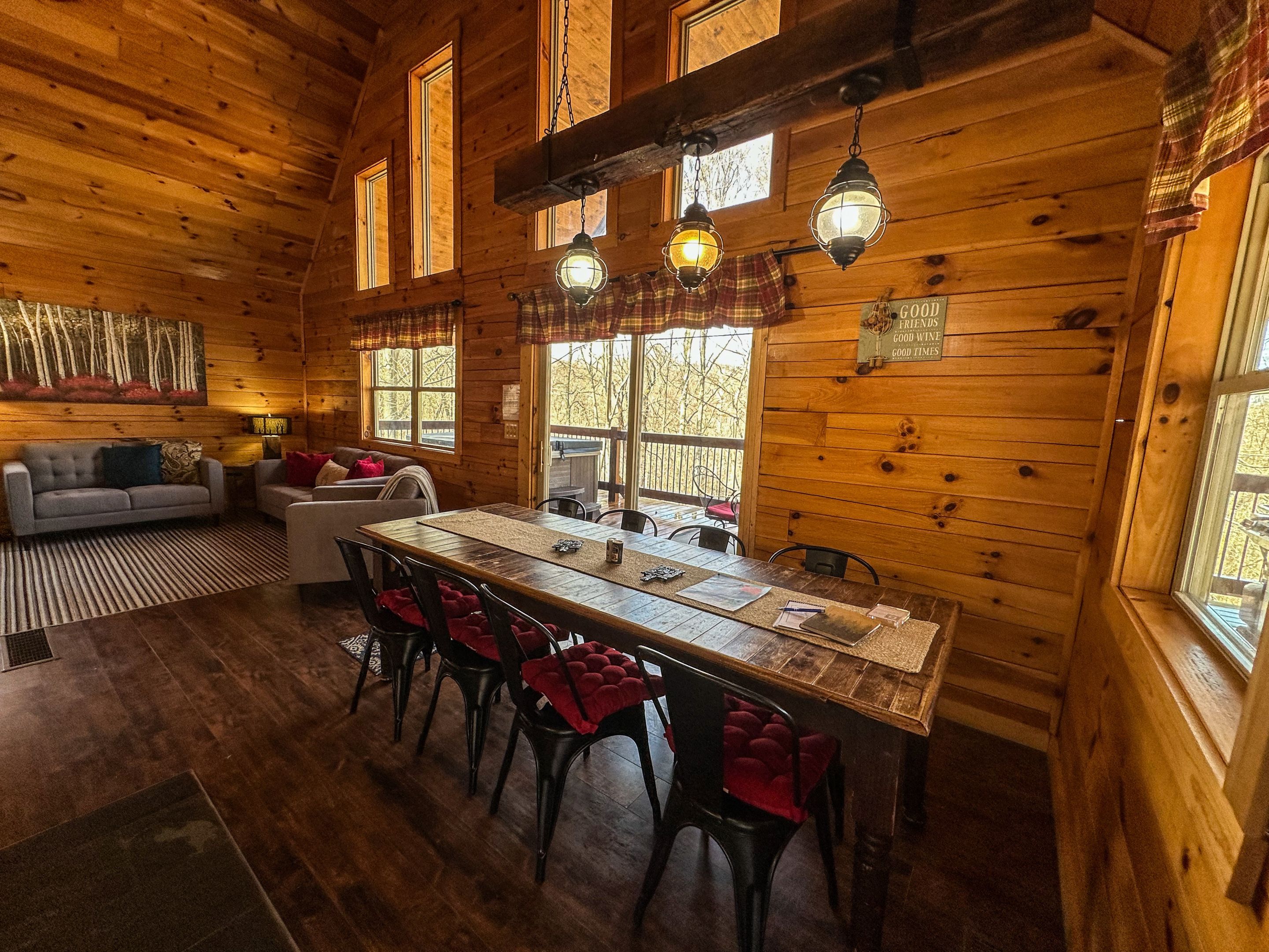 A wooden cabin interior with a dining table, chairs, a sofa, and a fireplace.