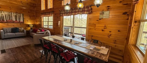 Interior de una cabaña de madera con una mesa de comedor, sillas, un sofá y una chimenea.