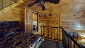 A wooden cabin bedroom with a bed, a ceiling fan, and a staircase. - Serendipitous Luxury Cabin with Forest Views, Hot Tub, mins from Hocking Hills (Logan)