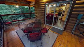 A wooden deck with a round table and chairs, a glass door leading to a kitchen, and a view of a forested area. - Serendipitous Luxury Cabin with Forest Views, Hot Tub, mins from Hocking Hills (Logan)
