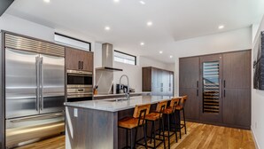 Une cuisine moderne dotée d’un îlot central, d’appareils électroménagers en acier inoxydable, de meubles de rangement en bois et d’un coin bar avec des tabourets.