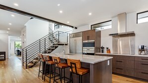 Une cuisine moderne dotée d’un îlot central, de tabourets de bar, d’appareils électroménagers en acier inoxydable et d’un escalier menant à un autre niveau.