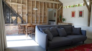 A room with a wooden ceiling, a grey sofa, a dining table with chairs, and a red rug. - The Cartlodge near Woodbridge - recently converted barn (Woodbridge)