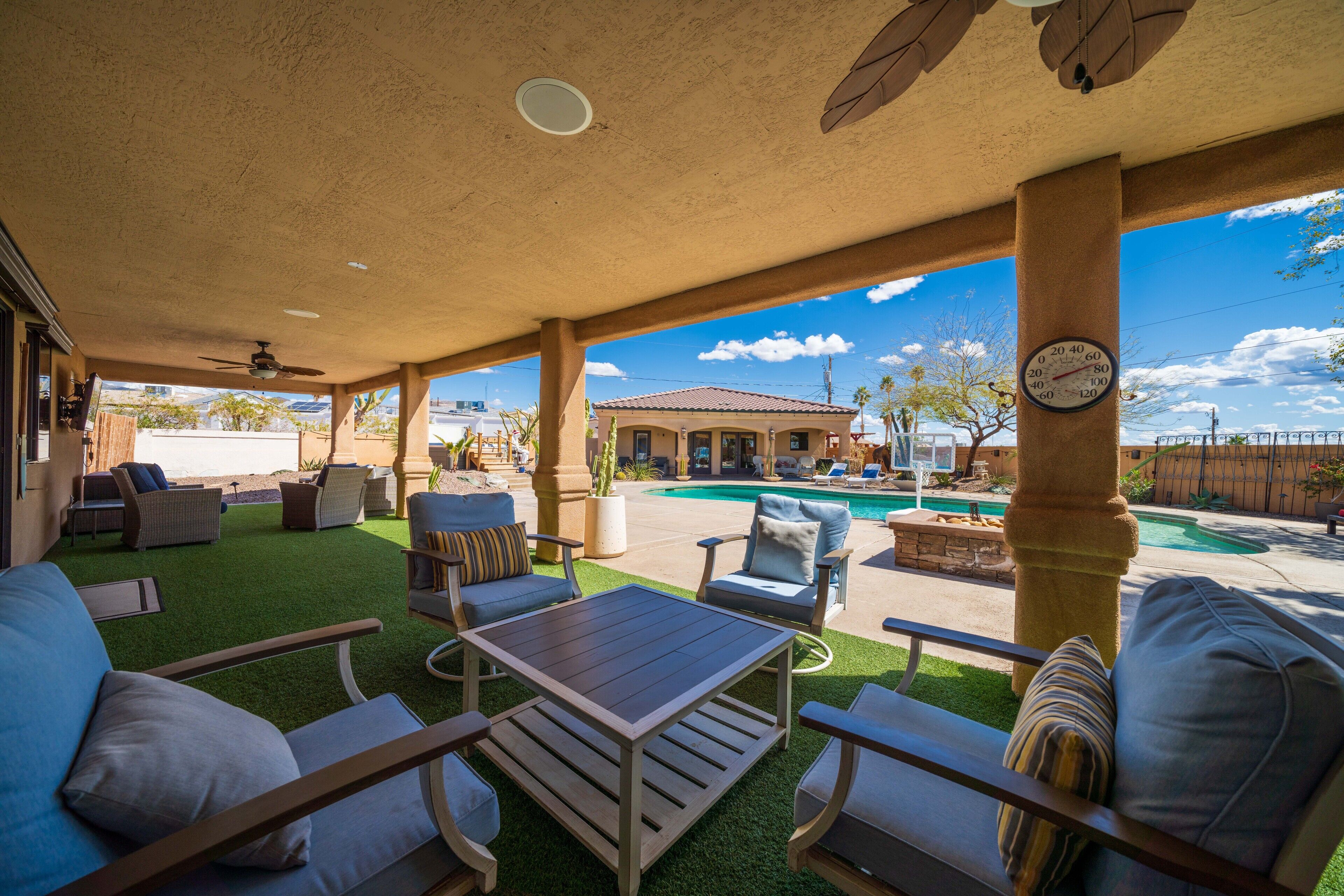 A covered patio area with outdoor furniture, a pool, and a view of a house in the background.