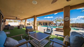 Un patio couvert aménagé avec du mobilier d’extérieur, une piscine et une vue sur une maison au loin.