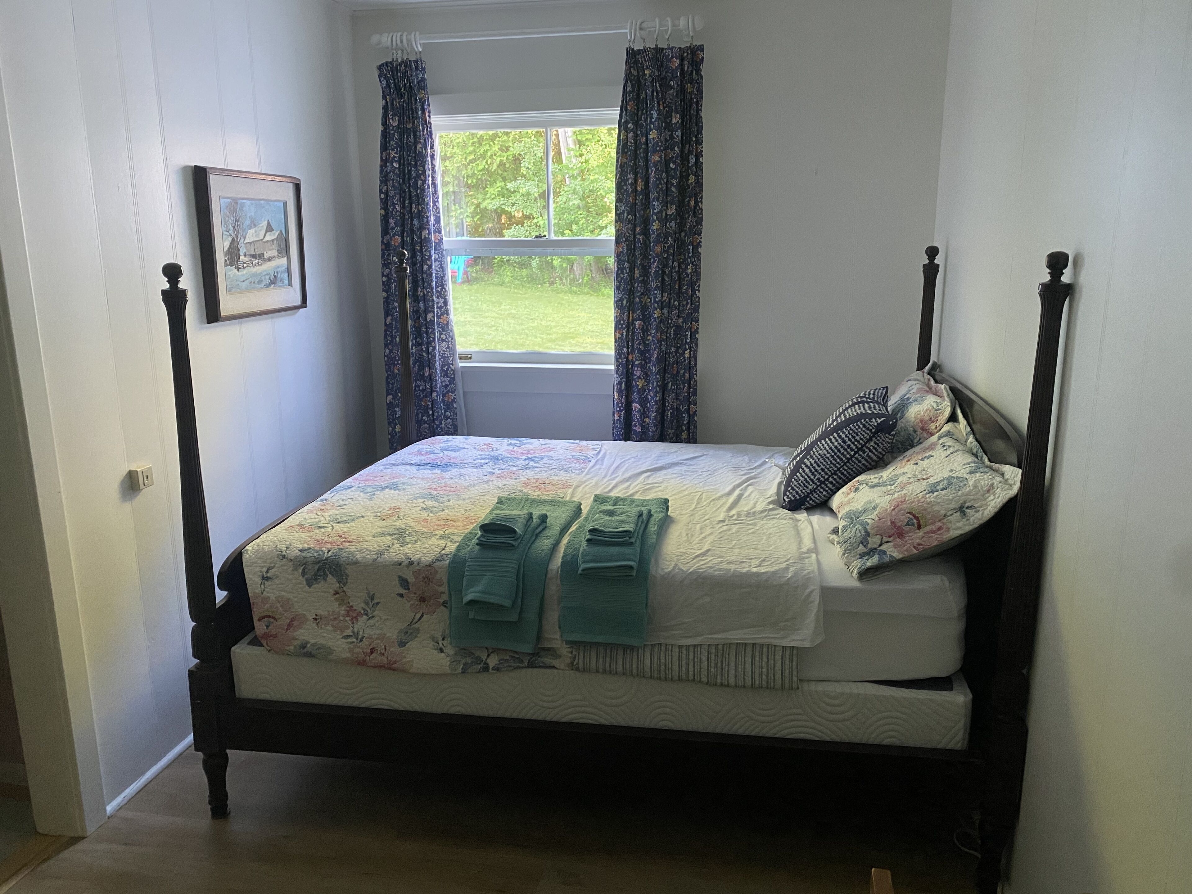 A neatly made bed with a floral bedspread, two green towels, and a pillow with a patterned cover.