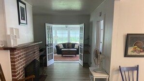 Un salon avec une cheminée, un coin repas avec une table et des chaises, et une vue sur un balcon accessible par une porte ouverte.