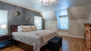 A bedroom with a large bed, a wooden dresser, and a ceiling light fixture. - Charming home with pet-friendly garden space and new hot tub! (Eugene)