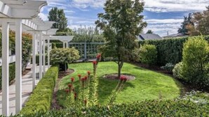 A well-maintained garden with a white pergola, neatly trimmed hedges, and a variety of shrubs and flowering plants. - Charming home with pet-friendly garden space and new hot tub! (Eugene)