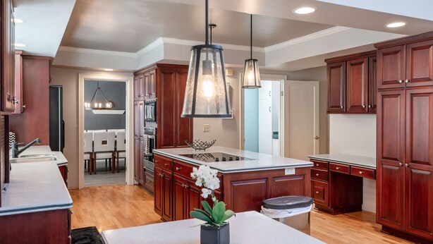 A modern kitchen with wooden cabinets, a central island, pendant lighting, and a view into the dining area. - Charming home with pet-friendly garden space and new hot tub! (Eugene)
