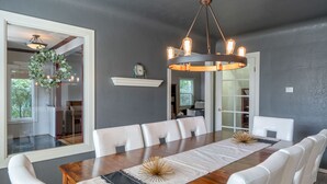 A dining area with a wooden table, white chairs, a chandelier, and a decorative wreath on the wall. - Charming home with pet-friendly garden space and new hot tub! (Eugene)