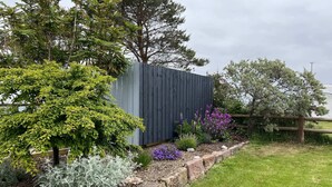 A garden with a stone retaining wall, various shrubs, and flowering plants. - Seaside cottage by a sandy beach - dolphins, golf, near Inverness and Loch Ness (Rosemarkie)
