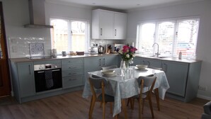 A modern kitchen with light blue cabinets, a dining table set for four, and a window with blinds. - Seaside cottage by a sandy beach - dolphins, golf, near Inverness and Loch Ness (Rosemarkie)