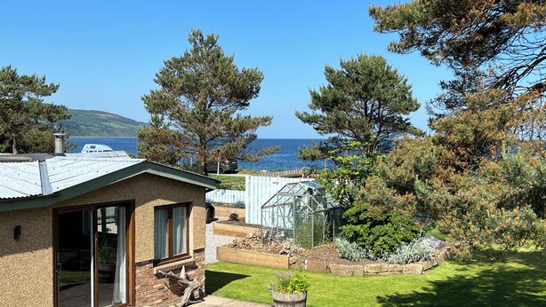 A house with a glass door entrance, a small garden with a wooden planter, and a greenhouse. - Seaside cottage by a sandy beach - dolphins, golf, near Inverness and Loch Ness (Rosemarkie)