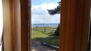 A view through a window with a wooden frame, leading to a grassy area with a paved path and a bench. - Seaside cottage by a sandy beach - dolphins, golf, near Inverness and Loch Ness (Rosemarkie)