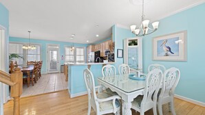 A modern kitchen with white cabinetry, a central island, and a dining area with white chairs and a glass table. - SUNSET ISLAND Spacious 5-BR - TONS of Amenities (Ocean City)