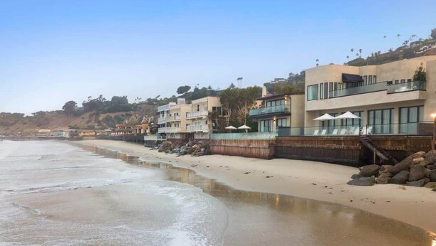 Une propriété située en bord de mer, avec une plage de sable, une côte rocheuse et des bâtiments modernes dotés de balcons.