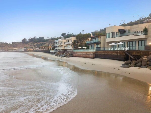 Um imóvel à beira-mar com uma praia de areia, uma costa rochosa e edifícios modernos com varandas.