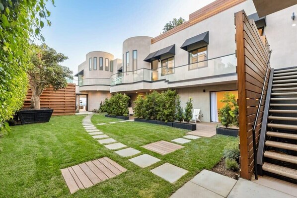 Un bâtiment moderne à plusieurs étages, doté d’une cour intérieure, d’une terrasse en bois et de plantes en pot.