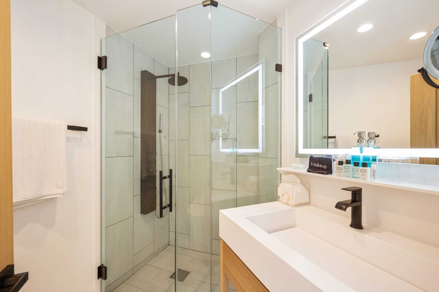 Un baño moderno con ducha envuelta en vidrio, un espejo grande y un tocador con artículos de aseo.