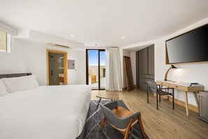 Une chambre d’hôtel équipée d’un lit, d’un bureau, d’une chaise, d’une télévision et d’une porte coulissante donnant sur un balcon.