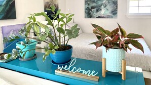 A room with a blue reception desk, a bed with white bedding, and various potted plants. - 🌿Peaceful Poolside Bungalow in Backyard Oasis🌿 (Austin)