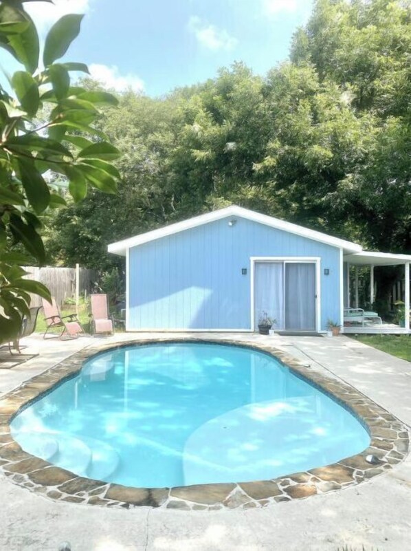 Enjoy an outdoor space with a swimming pool and deck, surrounded by lush trees and a charming shed.