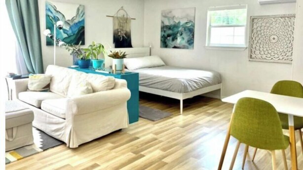 A modern, well-lit room with a bed, a sofa, a dining table, and chairs. There are abstract paintings on the walls and a window providing natural light. - 🌿Peaceful Poolside Bungalow in Backyard Oasis🌿 (Austin)