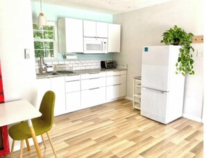 A modern kitchen with white cabinets, a microwave, a toaster, and a refrigerator. There is a green chair and a plant on the counter.
