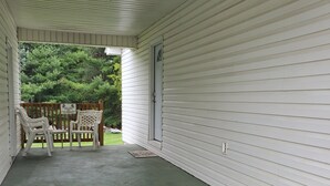 Un porche abrité avec un plancher en béton, un revêtement extérieur blanc et une porte donnant sur un jardin arrière.